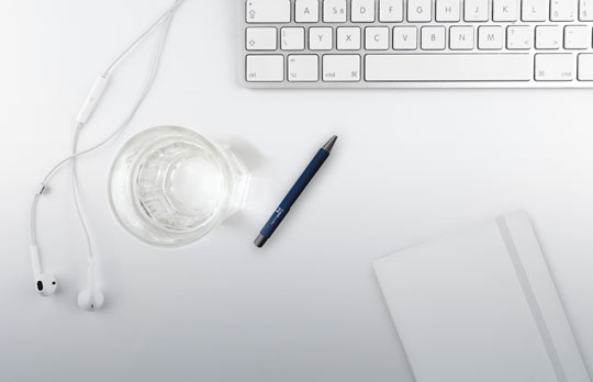 White desk with laptop, glass of water and headphones